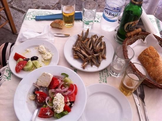 plates with Greek salad, small fish, bread, bottle of beer and water inside Saita tavern in Plaka